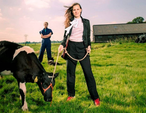 vrouw met een koe aangelijnd, een boer staat achter de koe en de vrouw