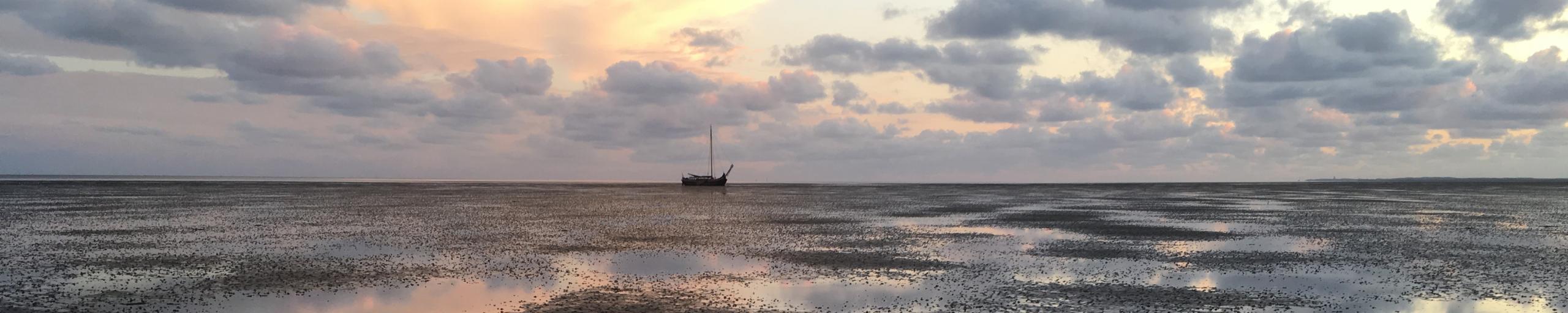 Varende zeilboot in de verte op het wad met ondergaande zon