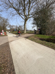 Het nieuwe betonnen fietspad waar een fietser oversteekt.